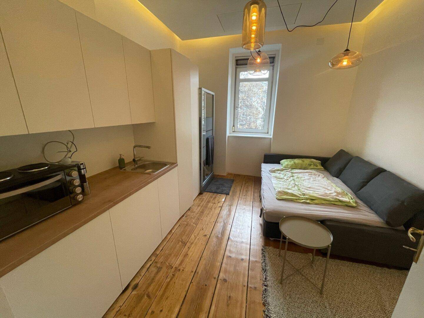 Helles Studio-Apartment mit Schlafsofa, Küchenzeile und Blick auf die Straße durch das Fenster.