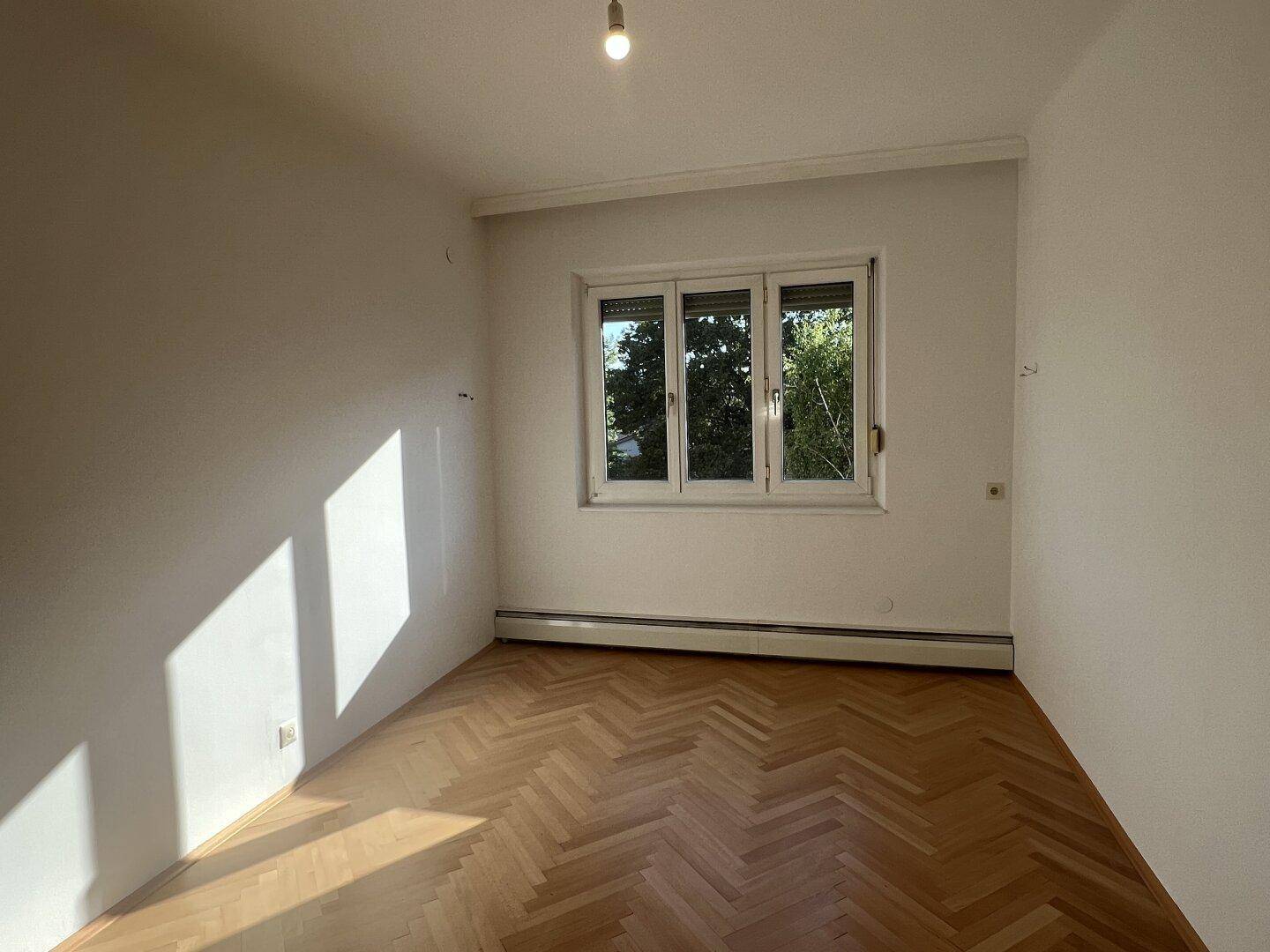 Lichtdurchfluteter Raum mit klassischem Fischgrätparkett und Blick ins Grüne.