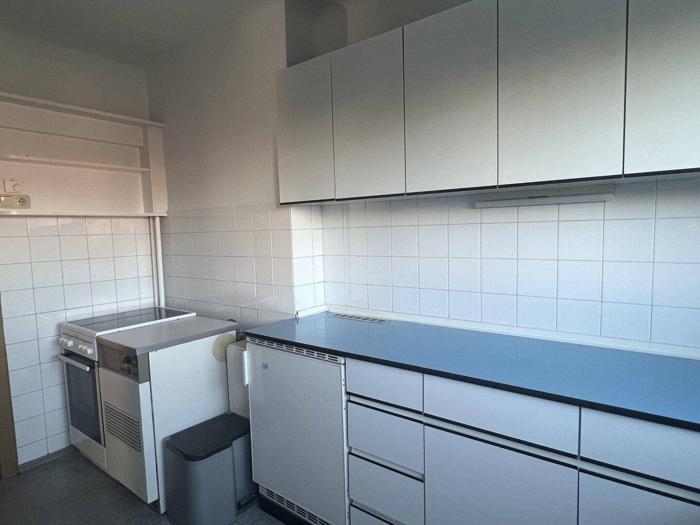 Küche mit weißen Einbauschränken, blauer Arbeitsplatte und klassischem Elektroherd.