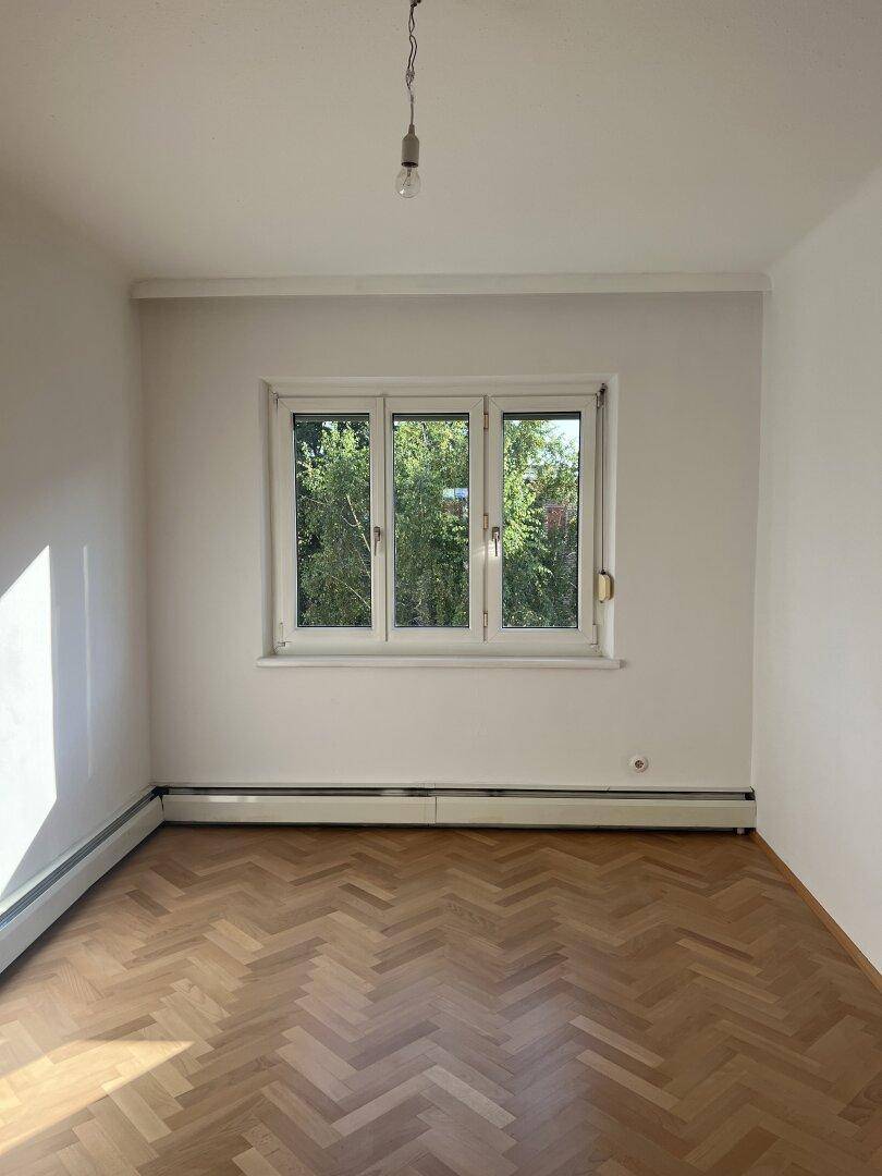 Geräumiger Raum mit Fischgrätparkettboden und viel Tageslicht durch das Fenster.