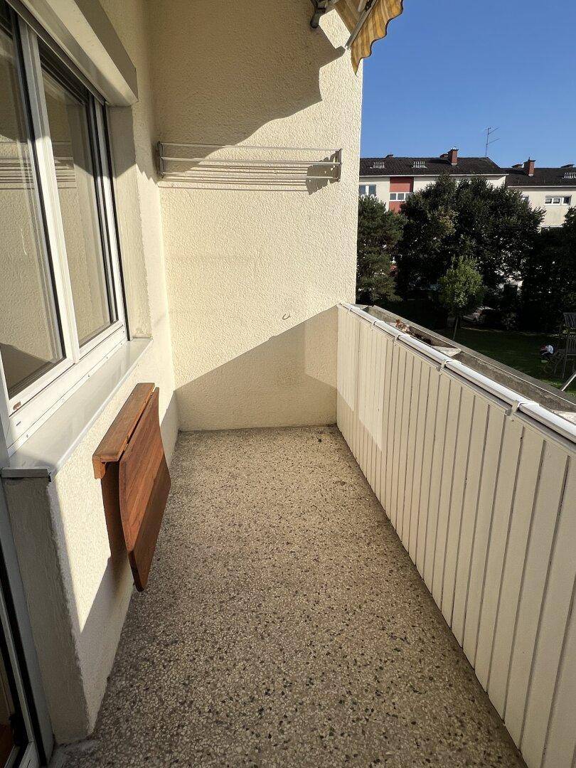 Schmaler Balkon mit Betonboden und einem praktischen Klapptisch an der Wand.