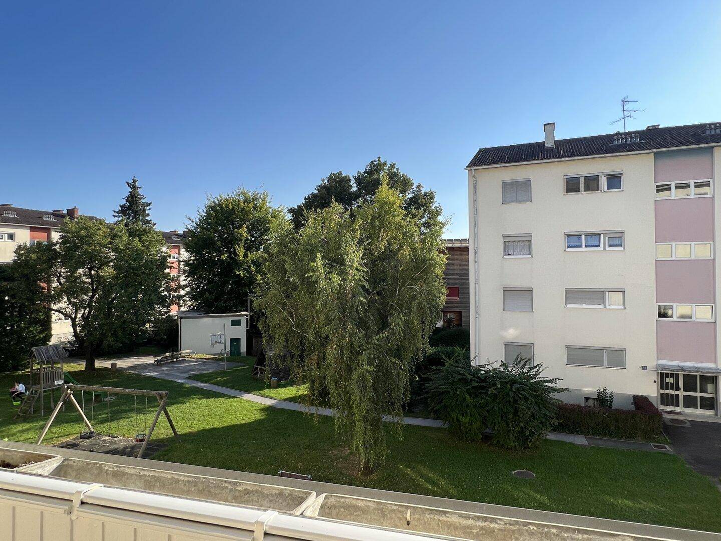 Blick vom Balkon auf den Gemeinschaftsgarten mit Spielplatz und umliegende Gebäude.