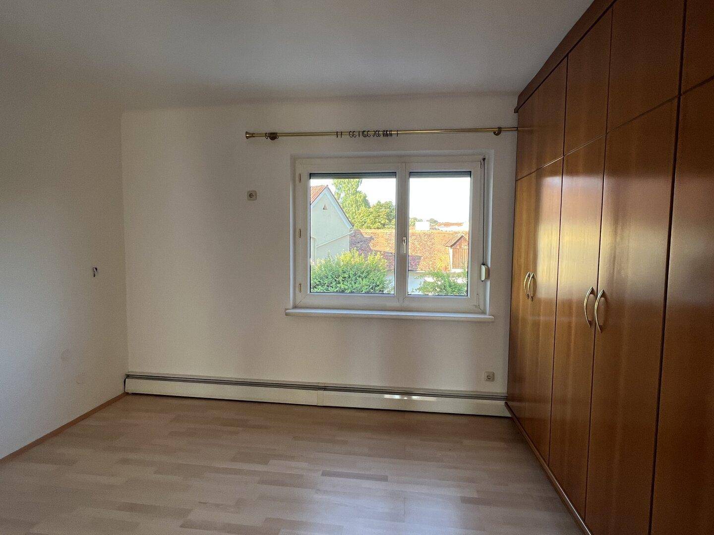 Schlafzimmer mit Laminatboden, Fenster und einem großen Einbauschrank aus Holz.