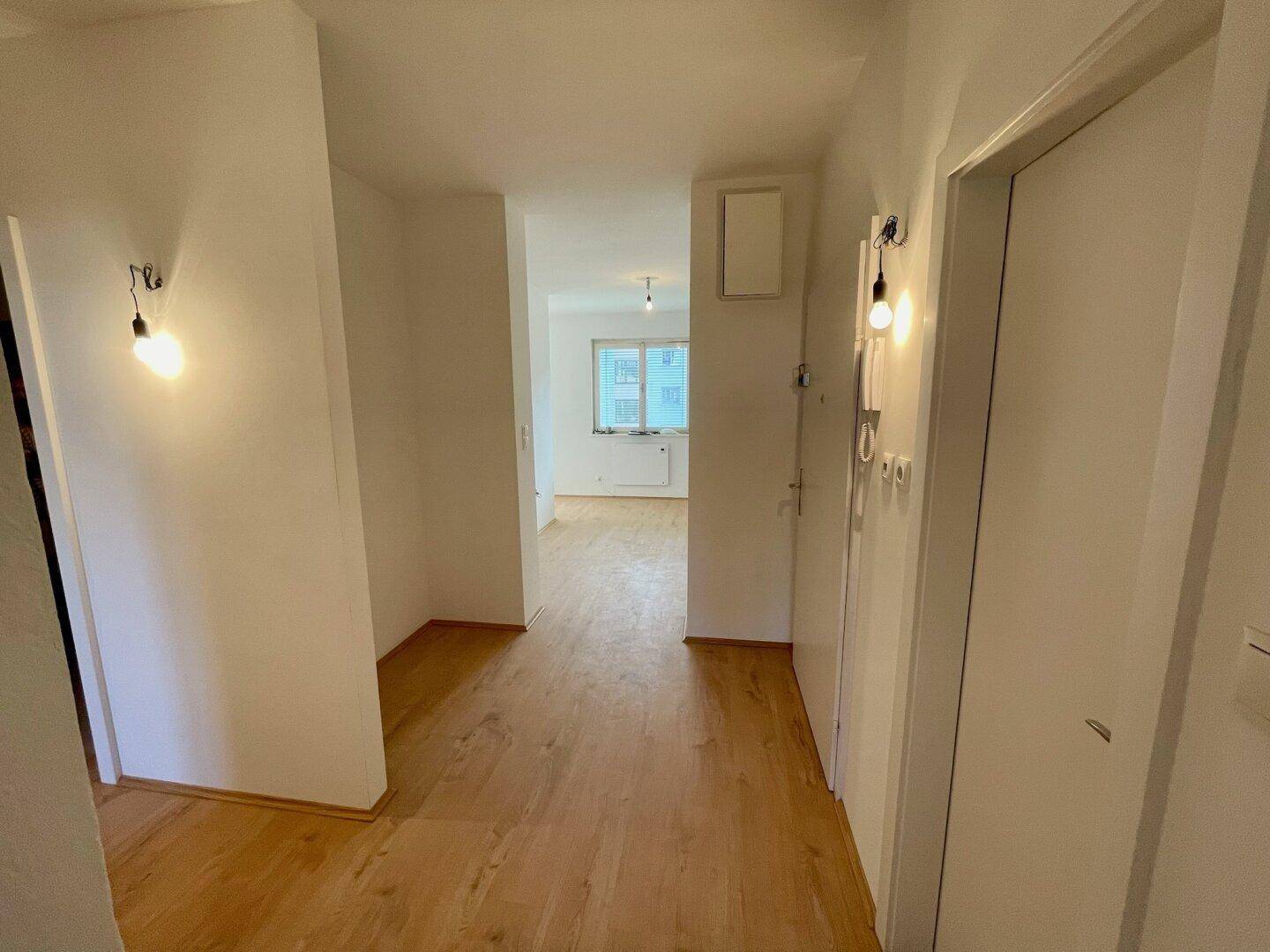 Heller Flur mit Holzfußboden, weißen Wänden und Blick in einen weiteren Raum.