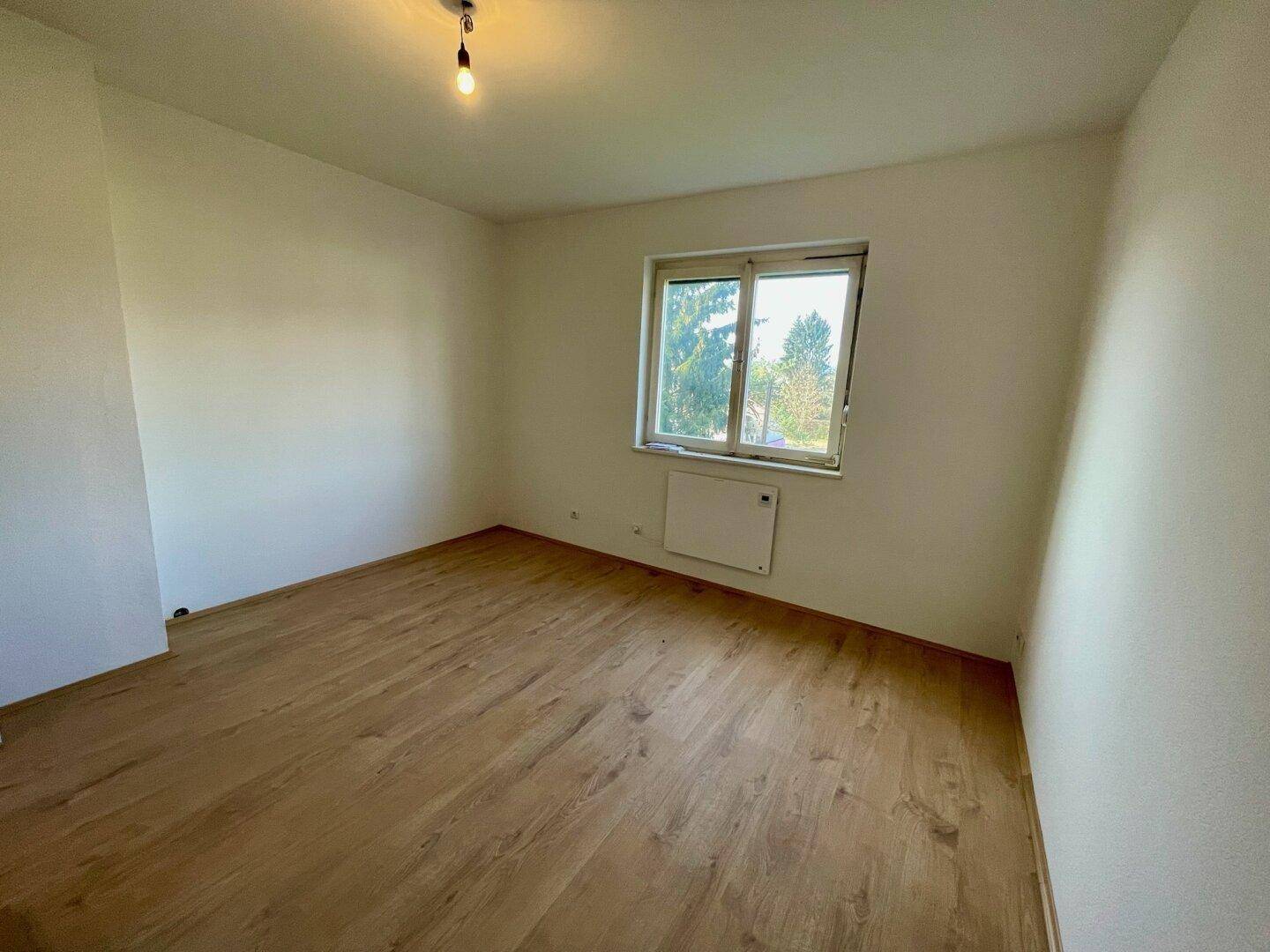 Helles Zimmer mit Holzfußboden und Fenster mit Blick ins Grüne.