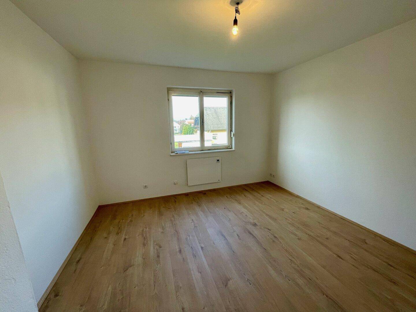 Geräumiges Zimmer mit Holzfußboden und Fenster mit Fernblick über die Dächer.