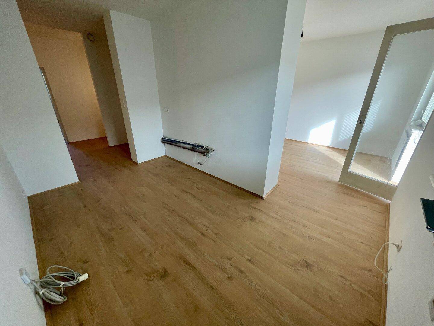 Geräumiger Raum mit Holzfußboden und sichtbaren Installationen für eine Küche.