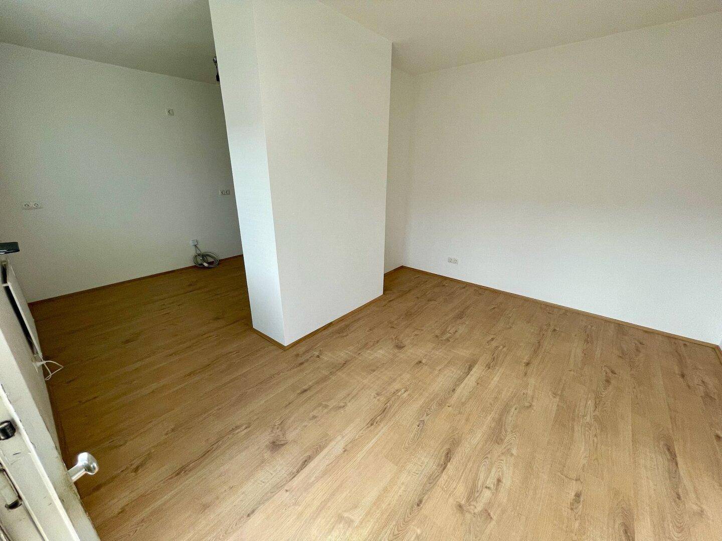Heller, leerer Raum mit Holzfußboden und weißen Wänden, bereit zur Gestaltung.