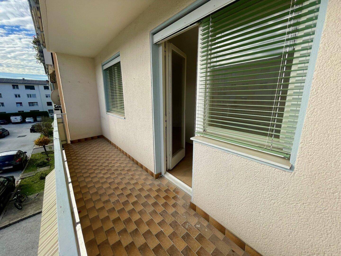 Balkon mit Fliesenboden und Blick auf die umliegenden Gebäude und die Straße.