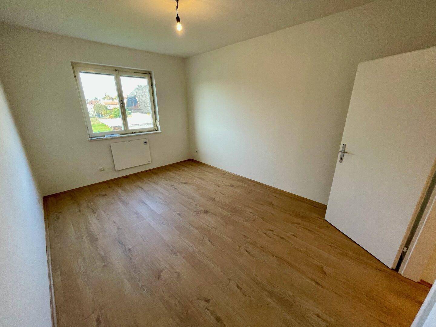 Helles Zimmer mit Holzfußboden, weißen Wänden und einem Fenster.