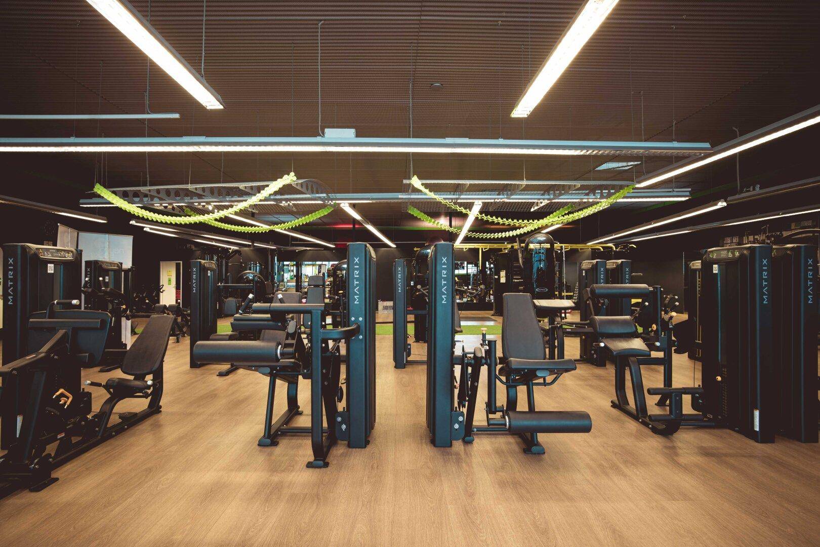 Großer Fitnessbereich mit zahlreichen modernen Trainingsgeräten und Holzboden.