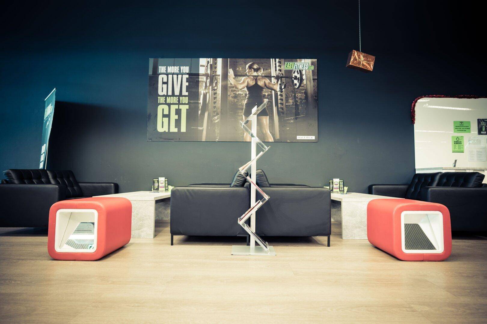 Gemütlicher Loungebereich mit schwarzen Sofas und roten Hockern, ideal zum Entspannen.