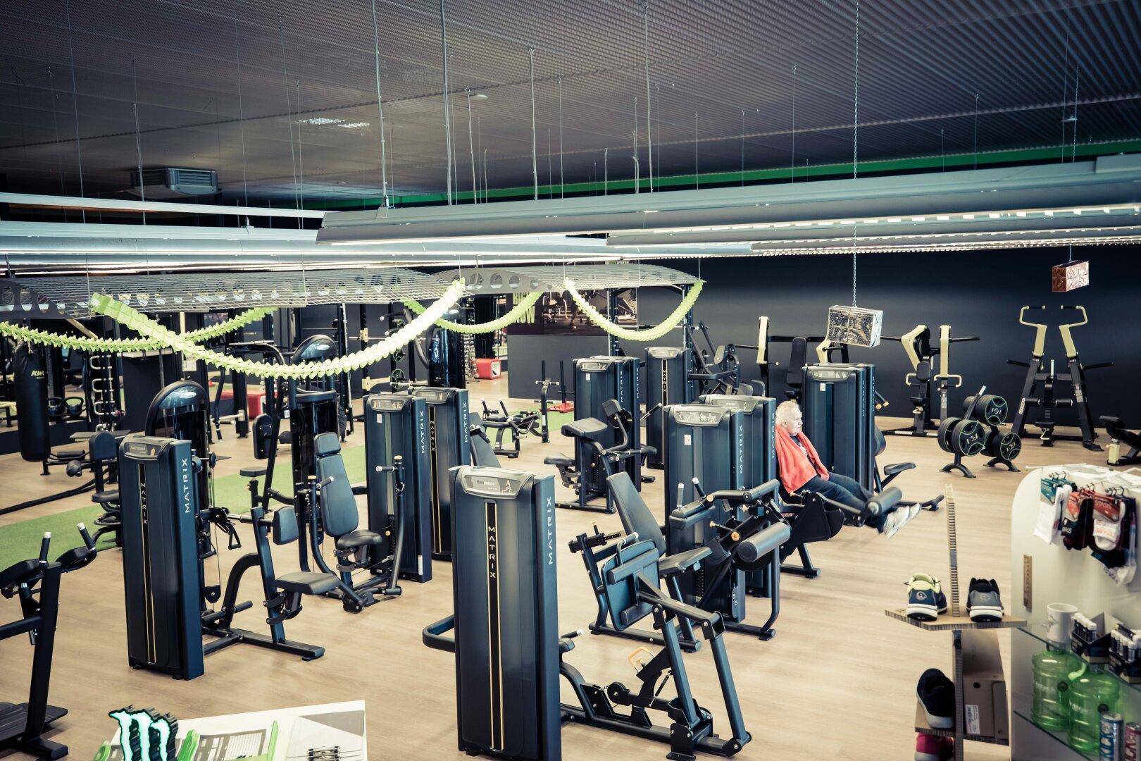 Weitläufiger Fitnessbereich mit einer Vielzahl von Trainingsgeräten und einem Mitglied beim Training.