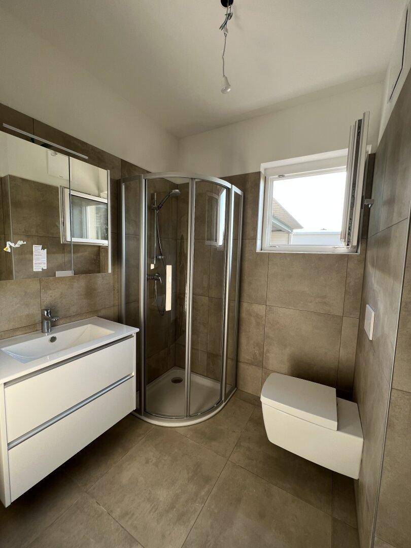 Helles Badezimmer mit Duschkabine, wandhängendem WC und Fenster für Tageslicht.
