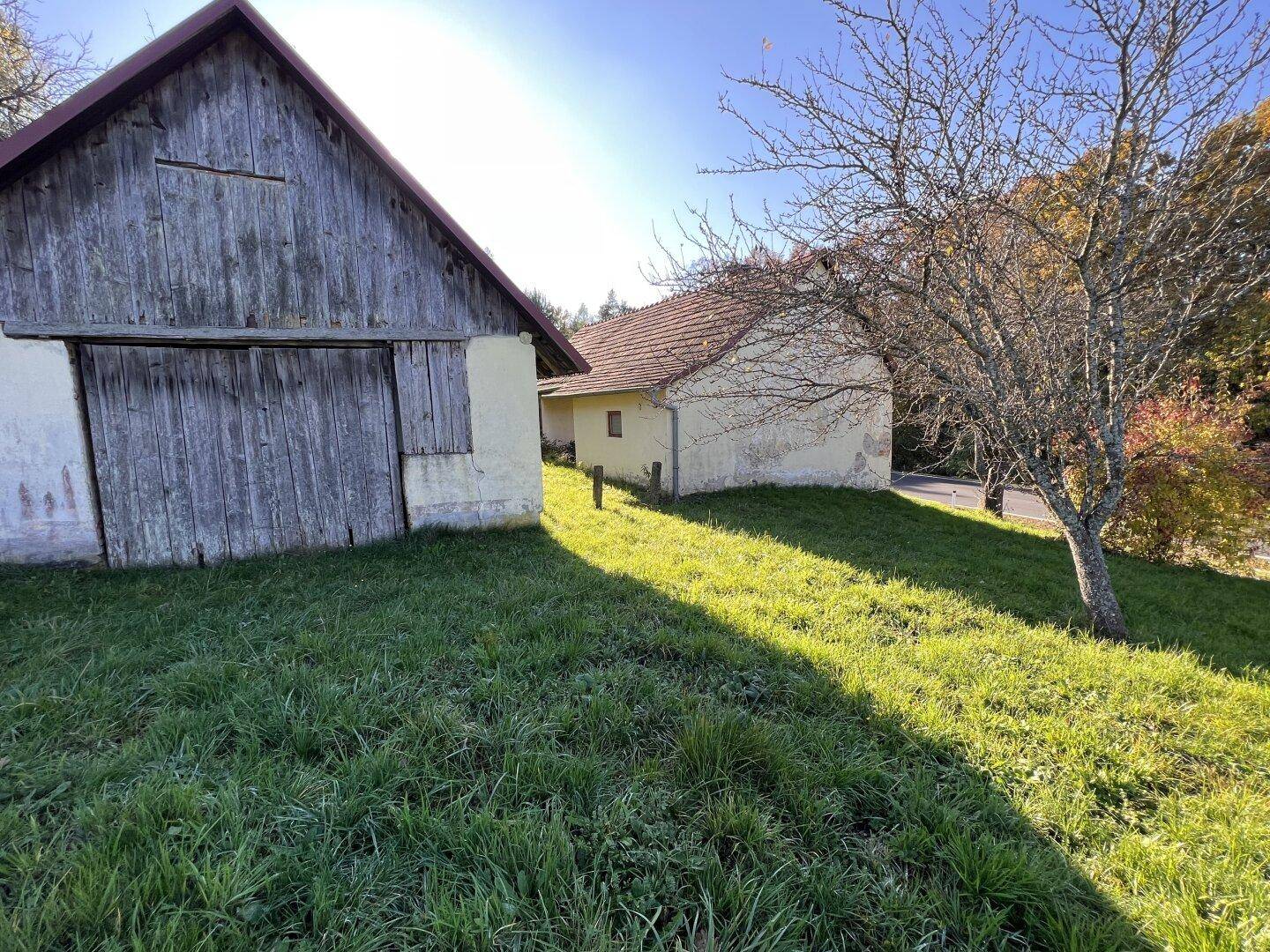 Zwei alte, verwitterte Gebäude auf einem sonnigen Hang mit herbstlicher Vegetation.