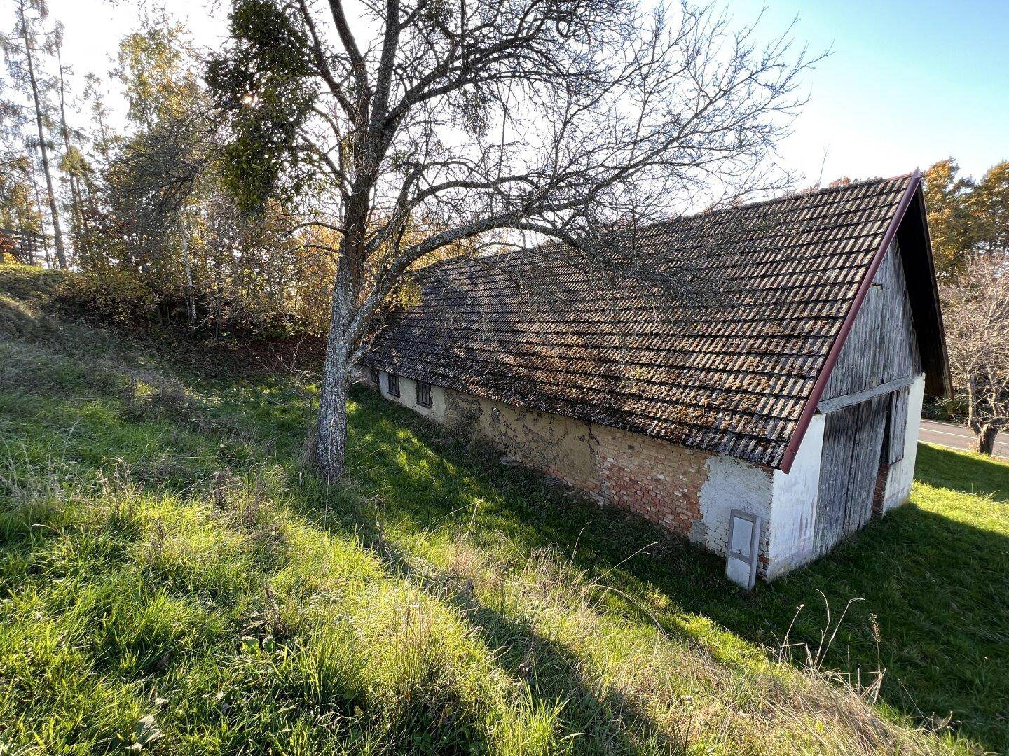 Altes, verfallenes Gebäude mit Ziegeldach und Holztüren auf einem grasbewachsenen Hang.