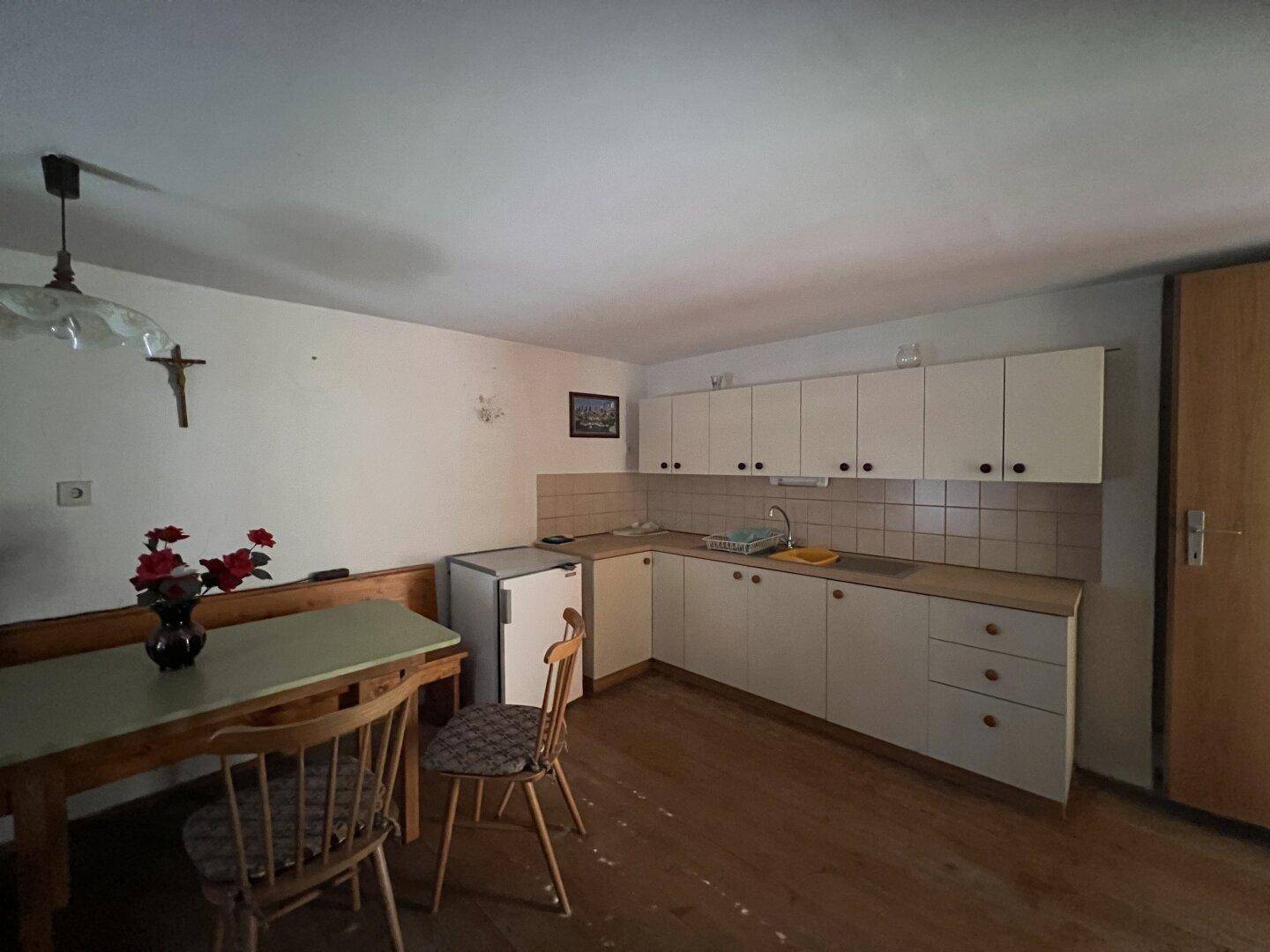 Einfache Küche mit weißen Schränken, Holzboden und einem Esstisch in einem älteren Stil.