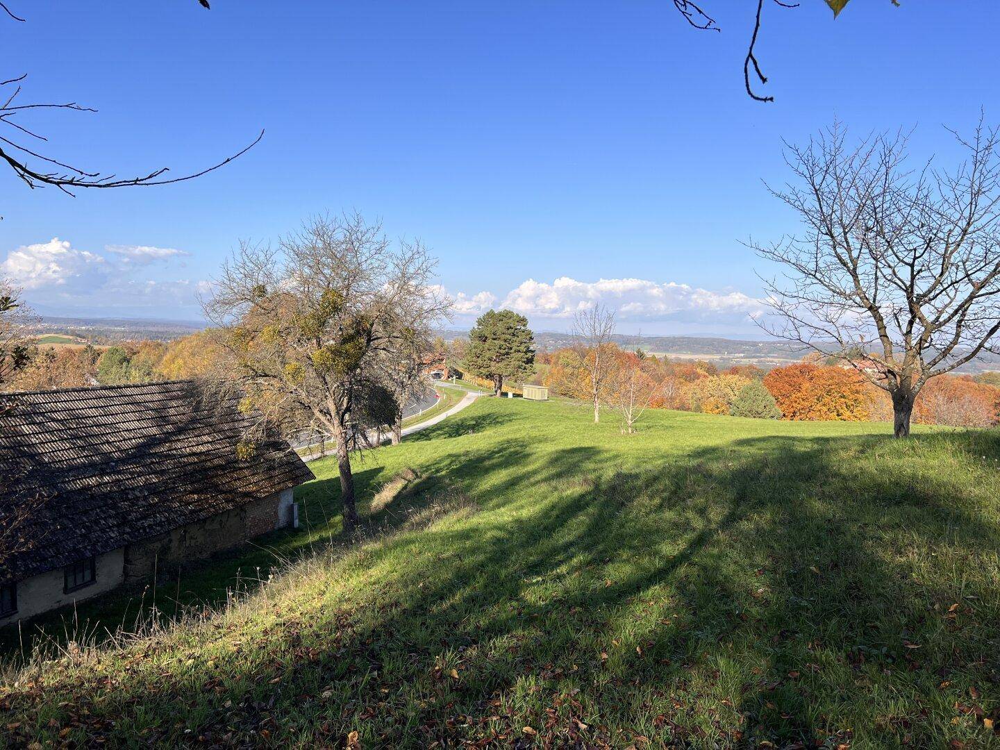 Panoramablick über eine weite, hügelige Landschaft mit einem alten Gebäude und herbstlichen Bäumen.