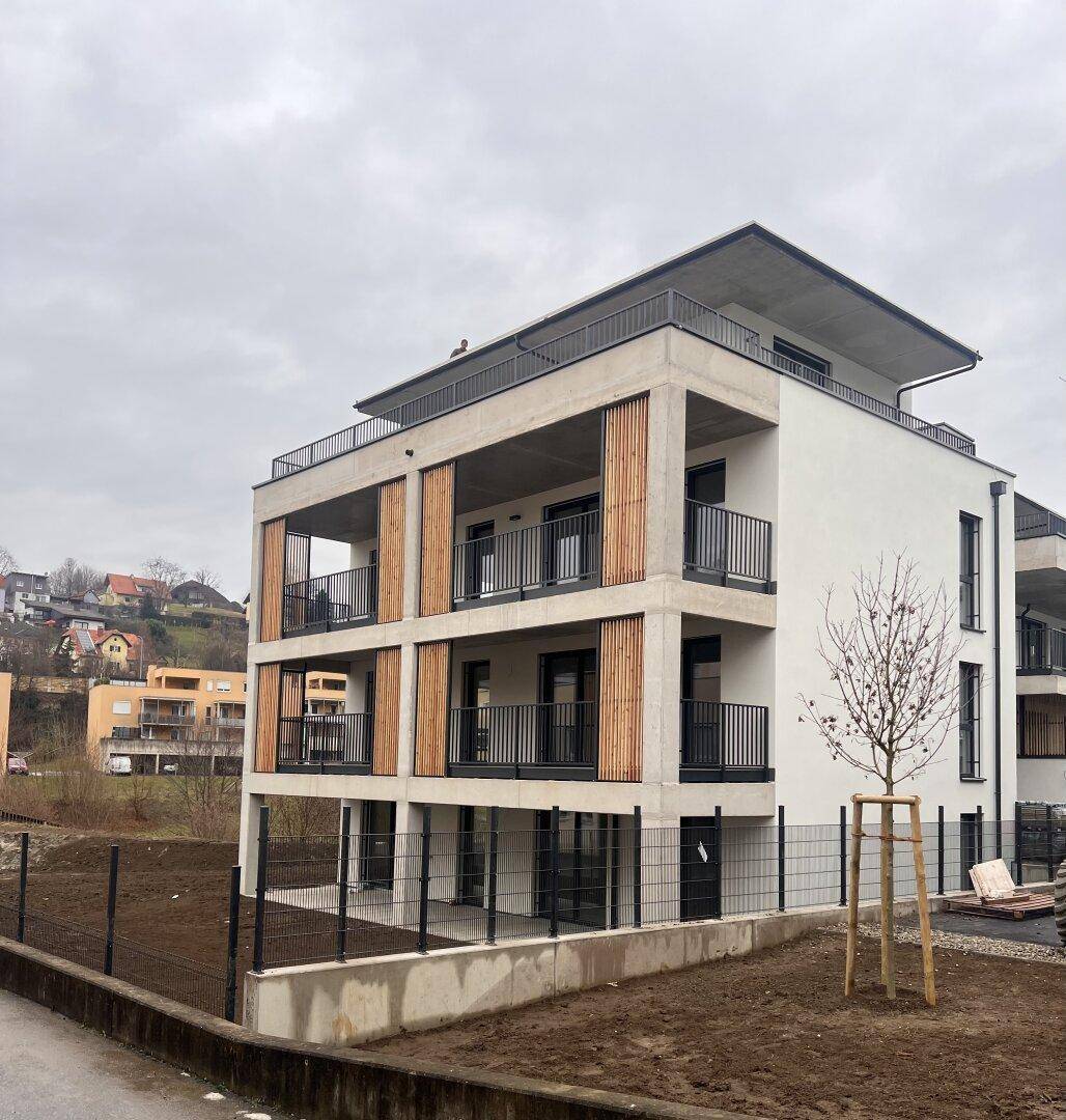 Modernes Wohngebäude mit Balkonen, Holzverkleidung und Betonstrukturen in einer hügeligen Umgebung.