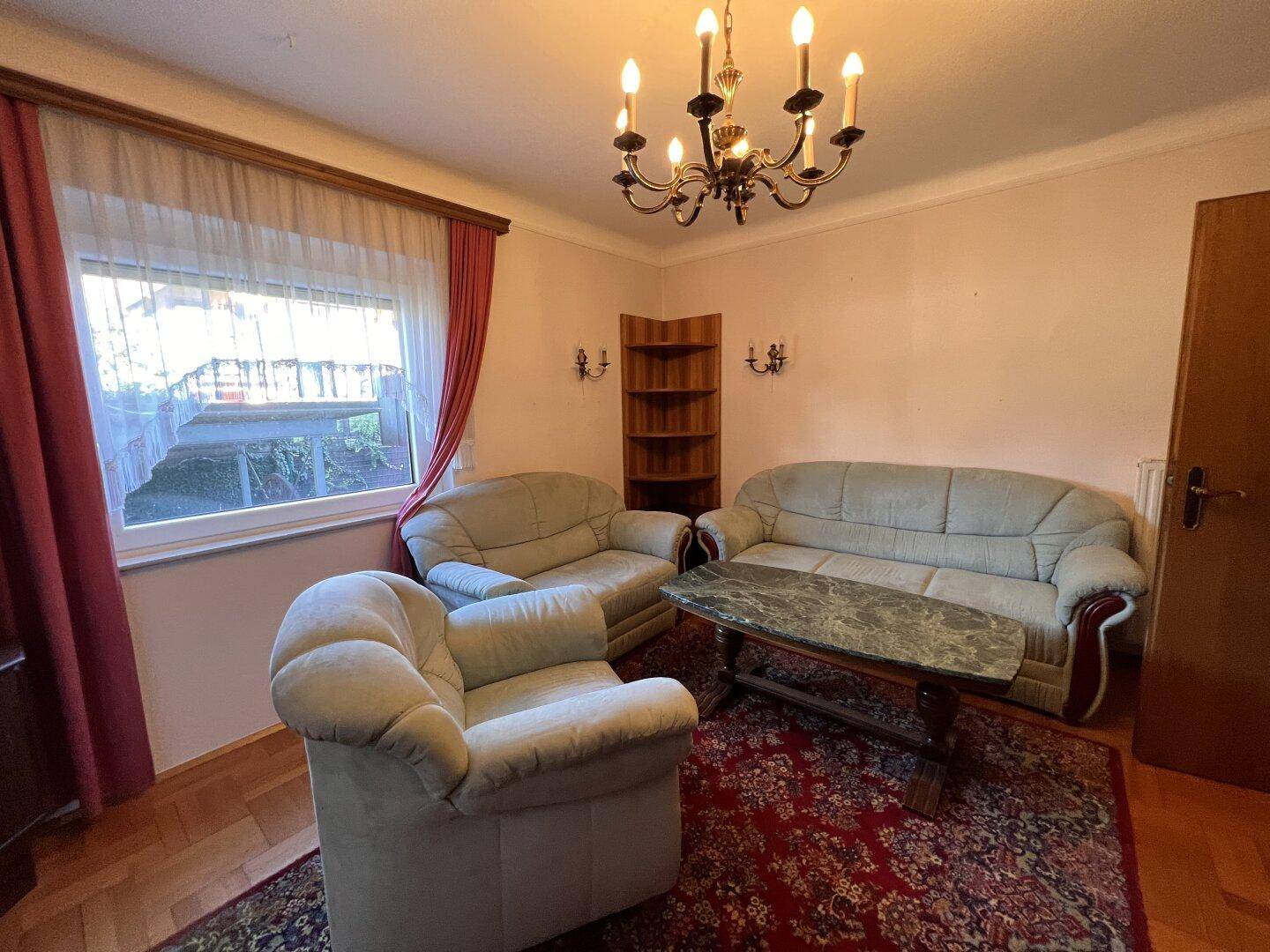 Gemütliches Wohnzimmer mit traditionellen Möbeln, Parkettboden und großem Fenster.