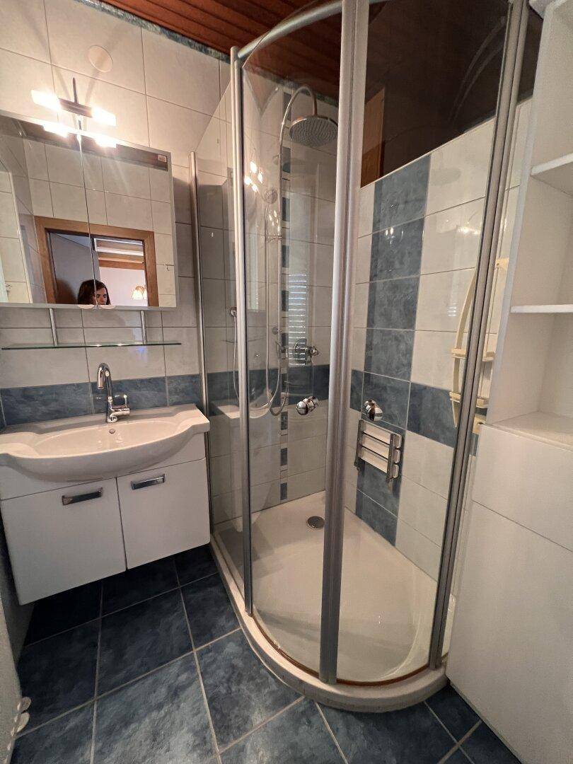 Modernes Badezimmer mit Duschkabine, Einzelwaschbecken und blau-weißen Fliesen.