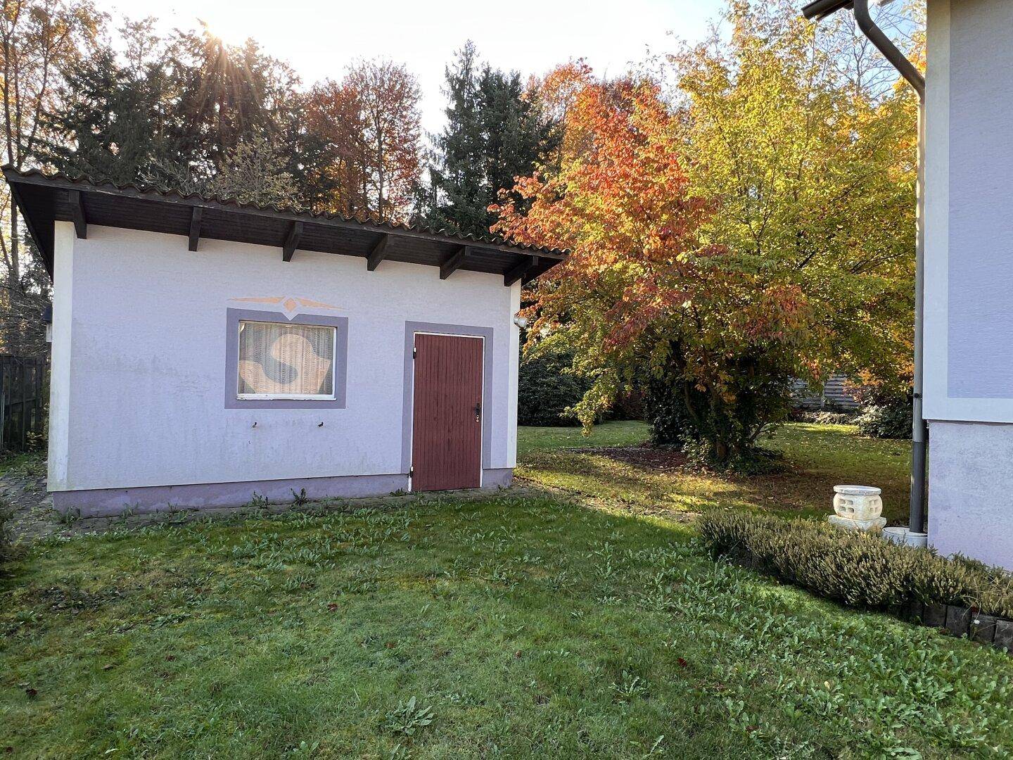 Kleines Nebengebäude im Garten mit Holztür und Fenster, umgeben von Rasen.