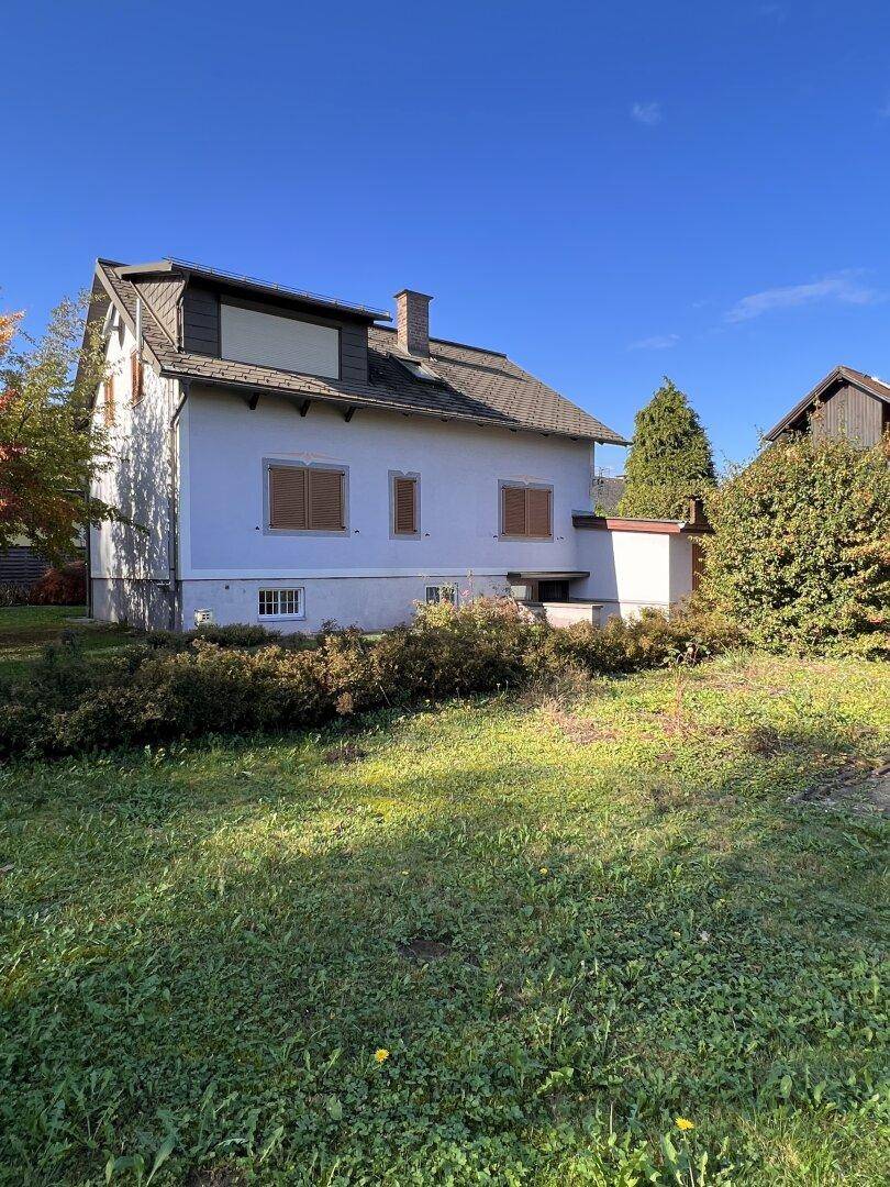 Rückansicht des Hauses mit Garten, Rasenfläche und blauem Himmel an einem sonnigen Tag.