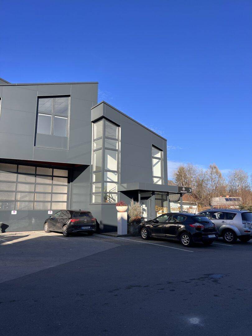 Modernes Geschäftsgebäude mit dunkler Fassade, großen Fenstern und Parkplätzen im Freien.