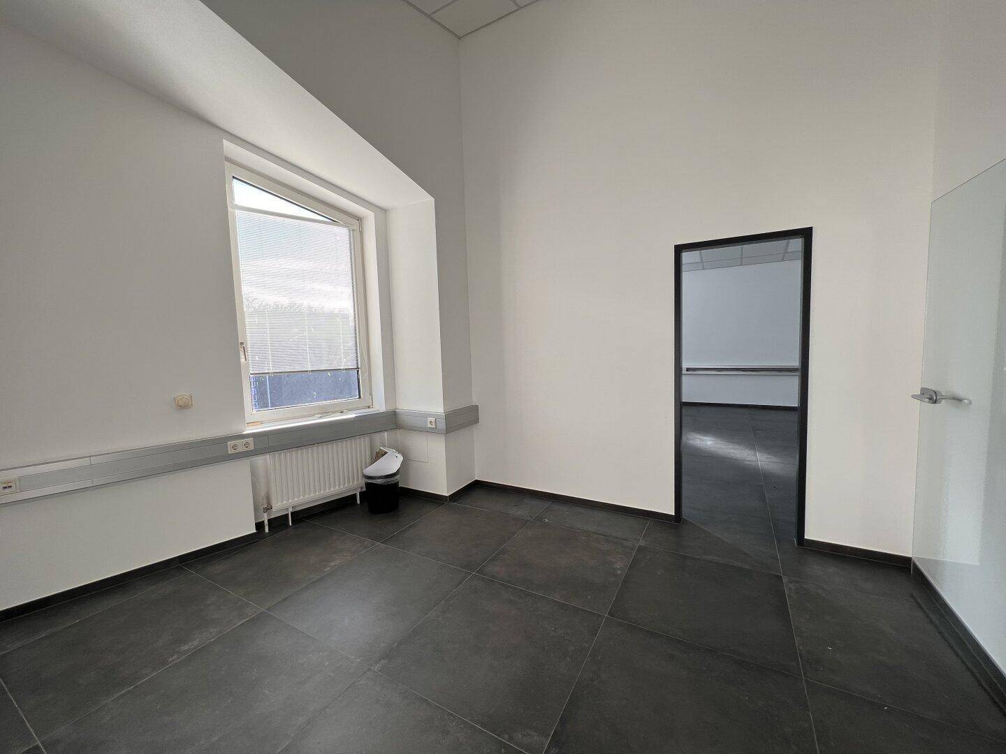 Helles Büro mit großem Fenster, dunklen Fliesen und Heizkörper in einem modernen Gebäude.
