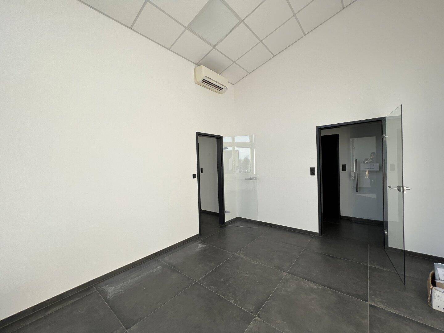 Geräumiges Büro mit Klimaanlage, dunklen Fliesen und einer modernen Glastür.