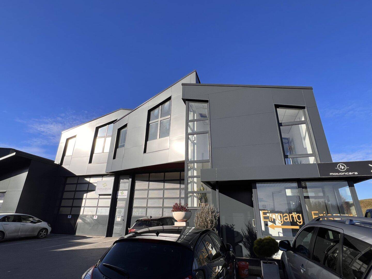 Modernes Geschäftsgebäude mit markanter Architektur, großen Glasflächen und Parkplätzen.