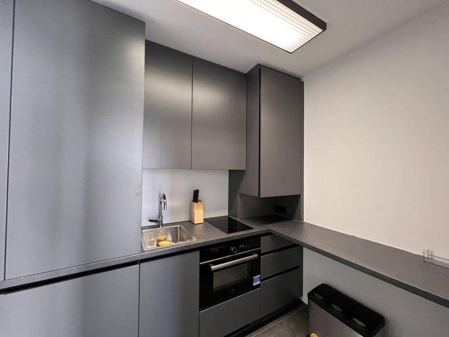 Moderne Küchenzeile in Grau mit Spüle, Kochfeld und Einbauofen in einem Bürogebäude.