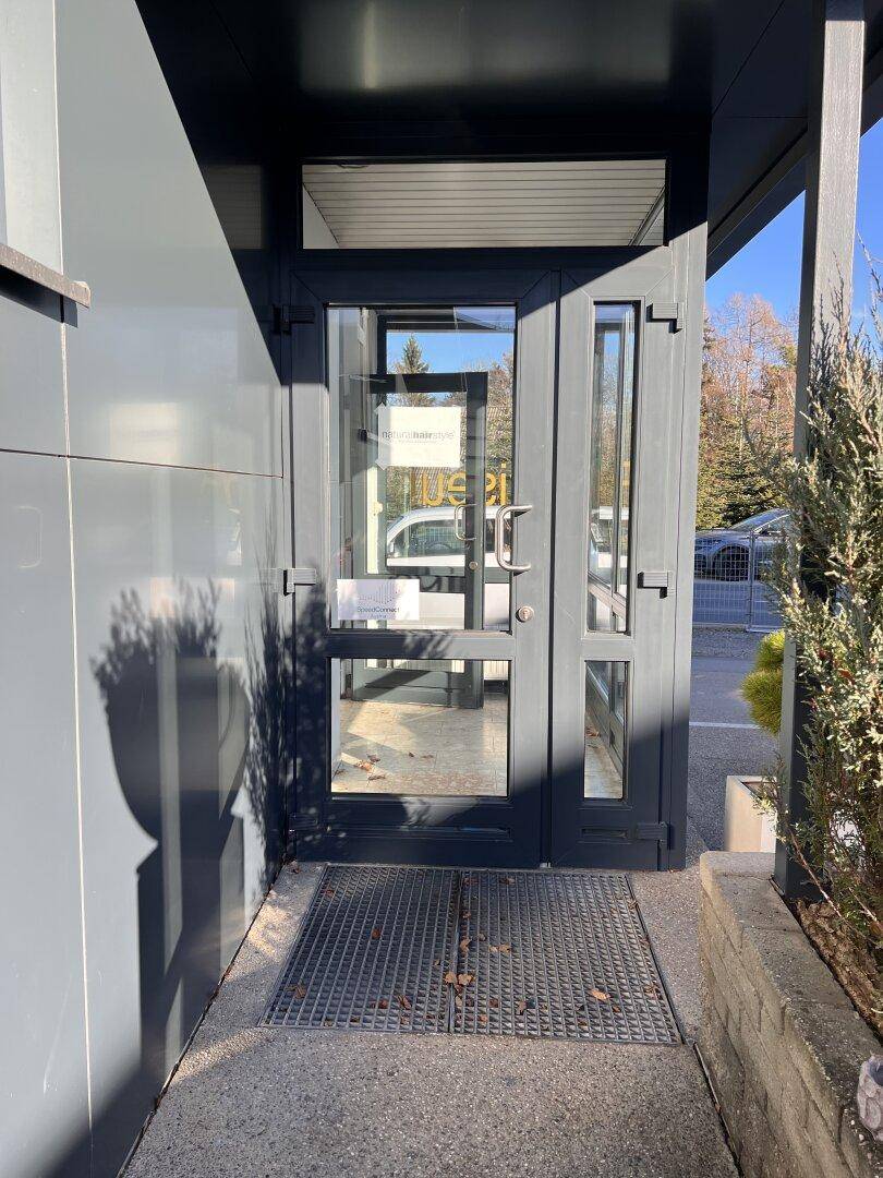 Moderner Gebäudeeingang mit Glastür und Metallgitterrost in einem Geschäftsgebäude.