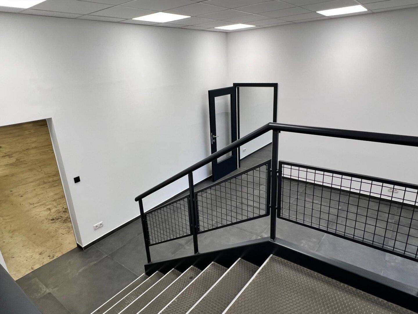 Moderne Treppe im Industriestil mit schwarzen Metallgeländern, die zu einem weiteren Bereich des Gebäudes führt.