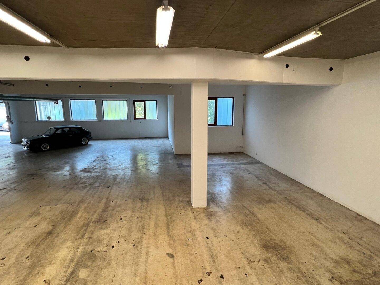 Spacious industrial hall with concrete floor, white walls, and a classic car parked in the background.