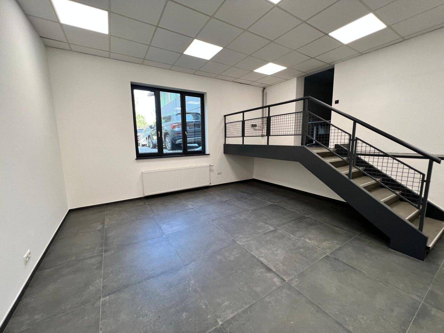 Moderner Büroraum mit dunklen Fliesen, einem großen Fenster und einer schwarzen Metalltreppe im Industriestil.