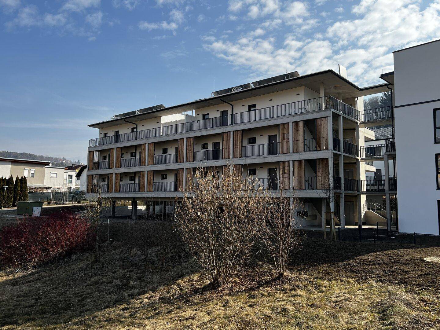 Weitläufige Ansicht des modernen Wohngebäudes mit Solaranlagen auf dem Dach und umliegender Grünfläche.