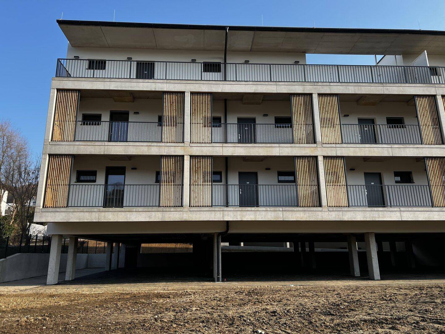 Frontansicht des Neubaus mit mehreren Balkonen, Holzlamellen an der Fassade und großzügigen Fensterfronten.