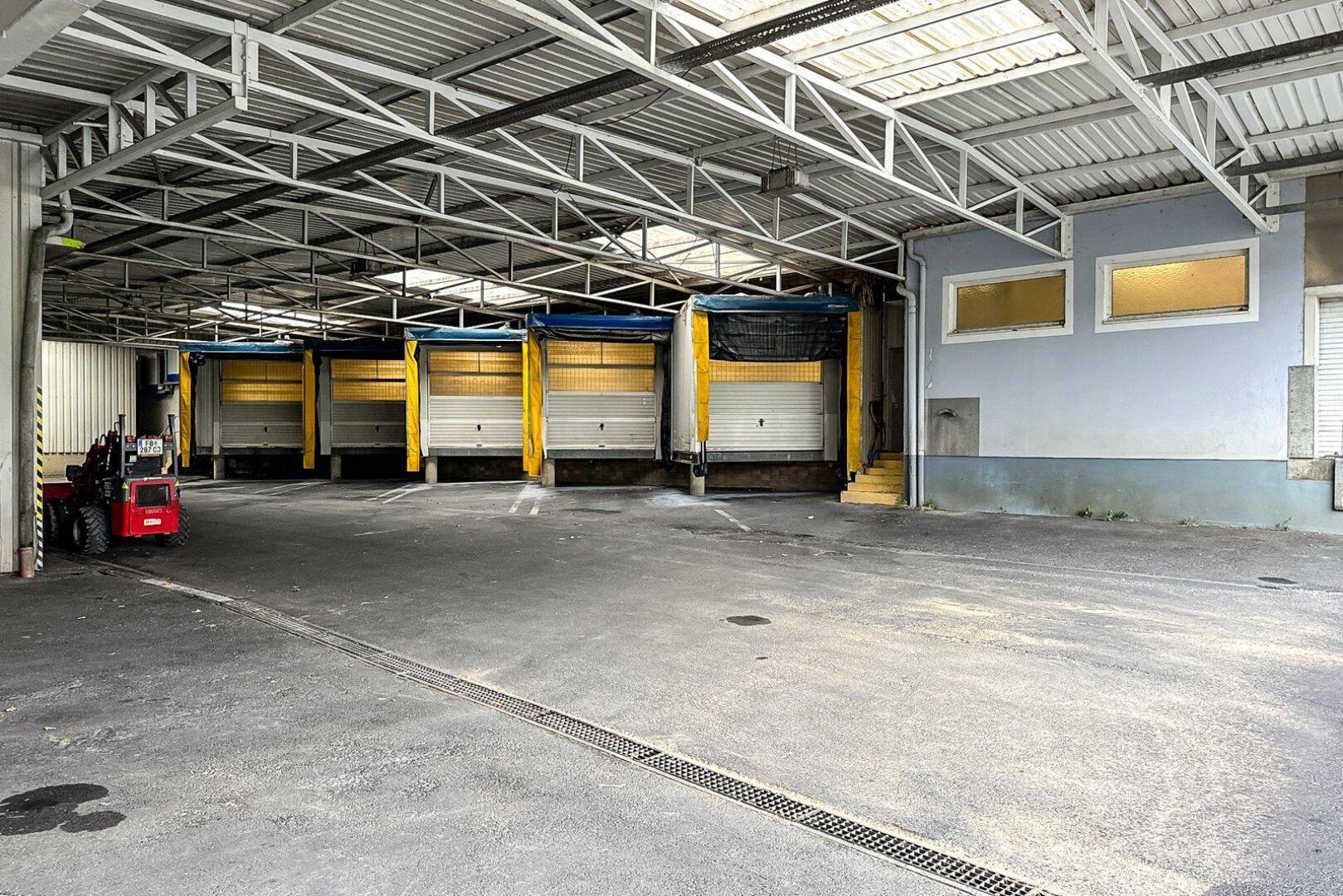 Großer überdachter Ladebereich mit mehreren Rolltoren, Betonboden, bereit für Logistik.