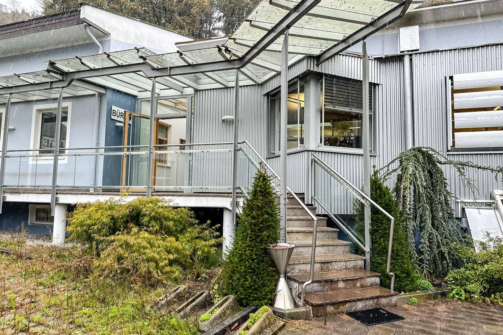 Detaillierte Ansicht des Eingangsbereichs mit Steintreppe, Glasgeländer und moderner Überdachung.