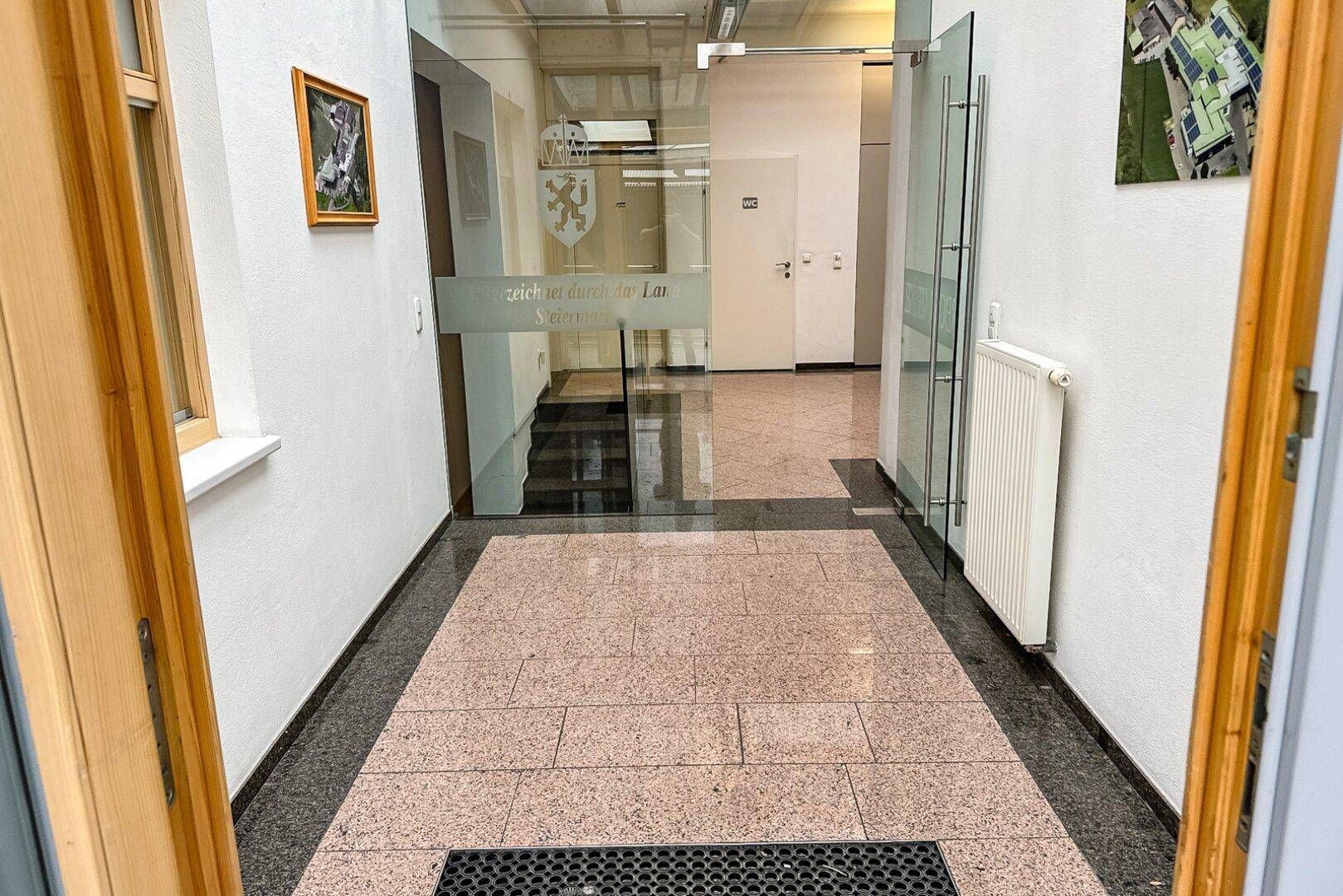 Heller Eingangsbereich mit Granitboden, Glastüren und einem Heizkörper, der zu weiteren Räumen führt.