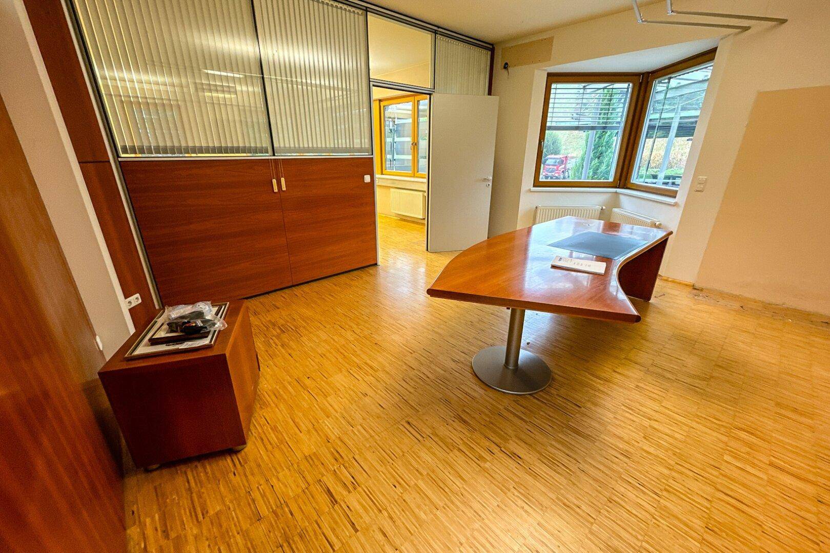 Modernes Büro mit elegantem Holzschreibtisch, Holzschränken und einer Glasabtrennung, die den Raum strukturiert.
