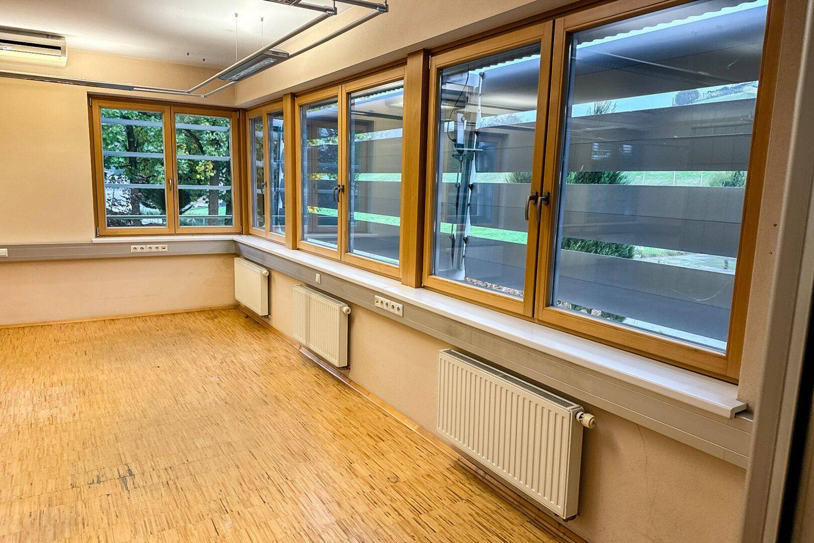 Ansicht des Büroraums mit einer langen Fensterfront, die viel Tageslicht und einen Blick ins Grüne bietet.