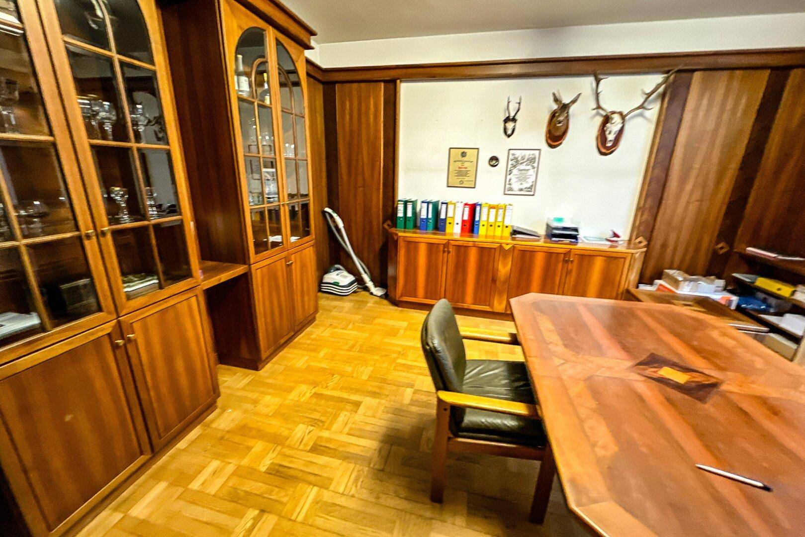 Traditionell eingerichtetes Büro mit dunklen Holzschränken, großem Schreibtisch und Jagdtrophäen an der Wand.