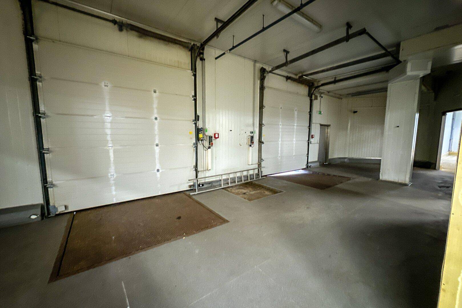 Großer Industrieraum mit zwei Rolltoren, Betonboden und hohen Decken, ideal als Lager oder Garage.