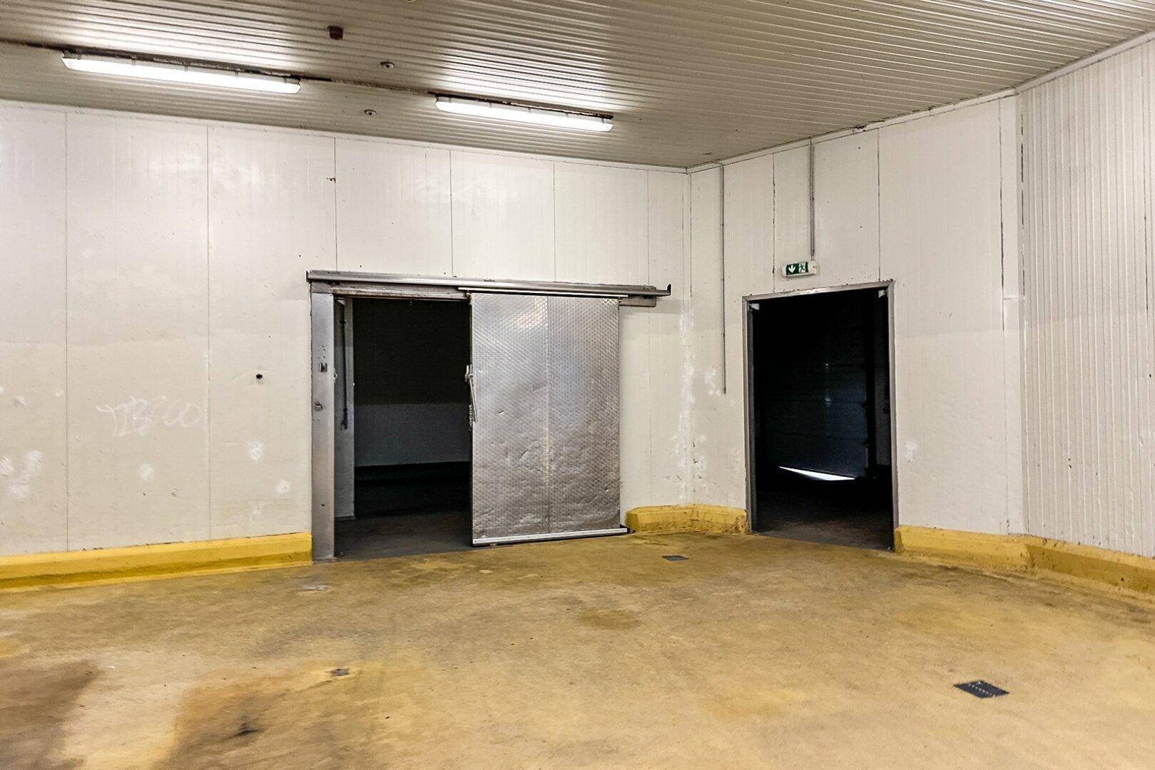 Industrieraum mit großer Metallschiebetür, normaler Tür und gelb-orangefarbenem Betonboden, funktional und geräumig.