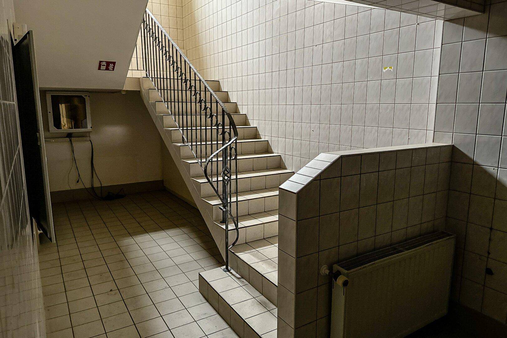Gefliestes Treppenhaus mit Metallgeländer und Heizkörper, das verschiedene Etagen miteinander verbindet.