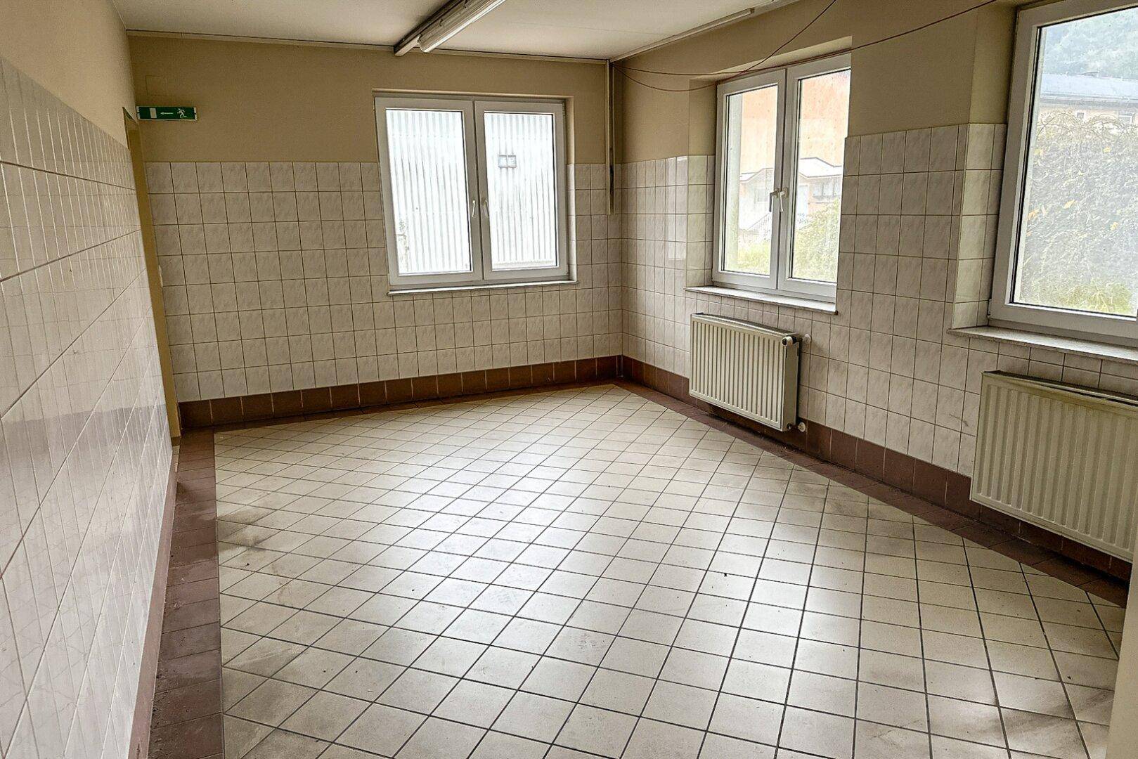 Raum mit gefliesten Wänden und Boden, mehreren Fenstern und Heizkörpern, geeignet als Wirtschaftsraum.