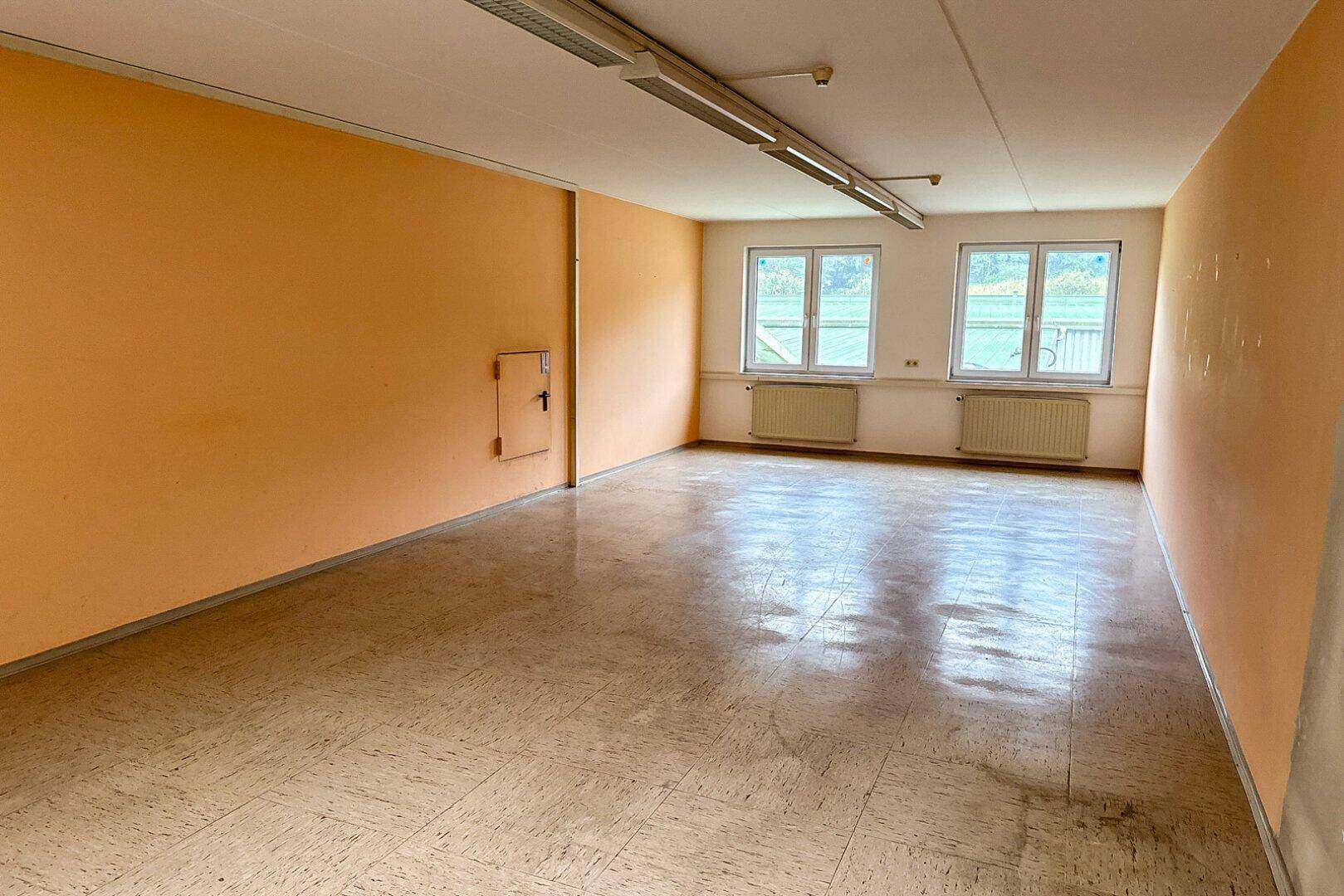 Leerer Raum mit orangefarbenen Wänden, Linoleumboden und zwei Fenstern, die den Raum erhellen.