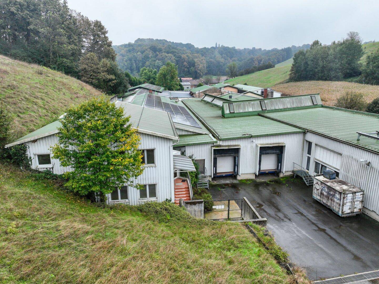 Luftaufnahme des Industriekomplexes mit weißen Gebäuden, grünen Dächern und Laderampen, eingebettet in grüne Hügel.